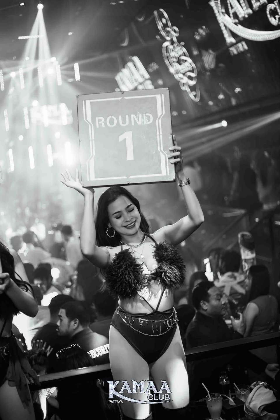 Black-and-white photo of a show performer holding a 'Round 1' card at Kamaa Club Pattaya